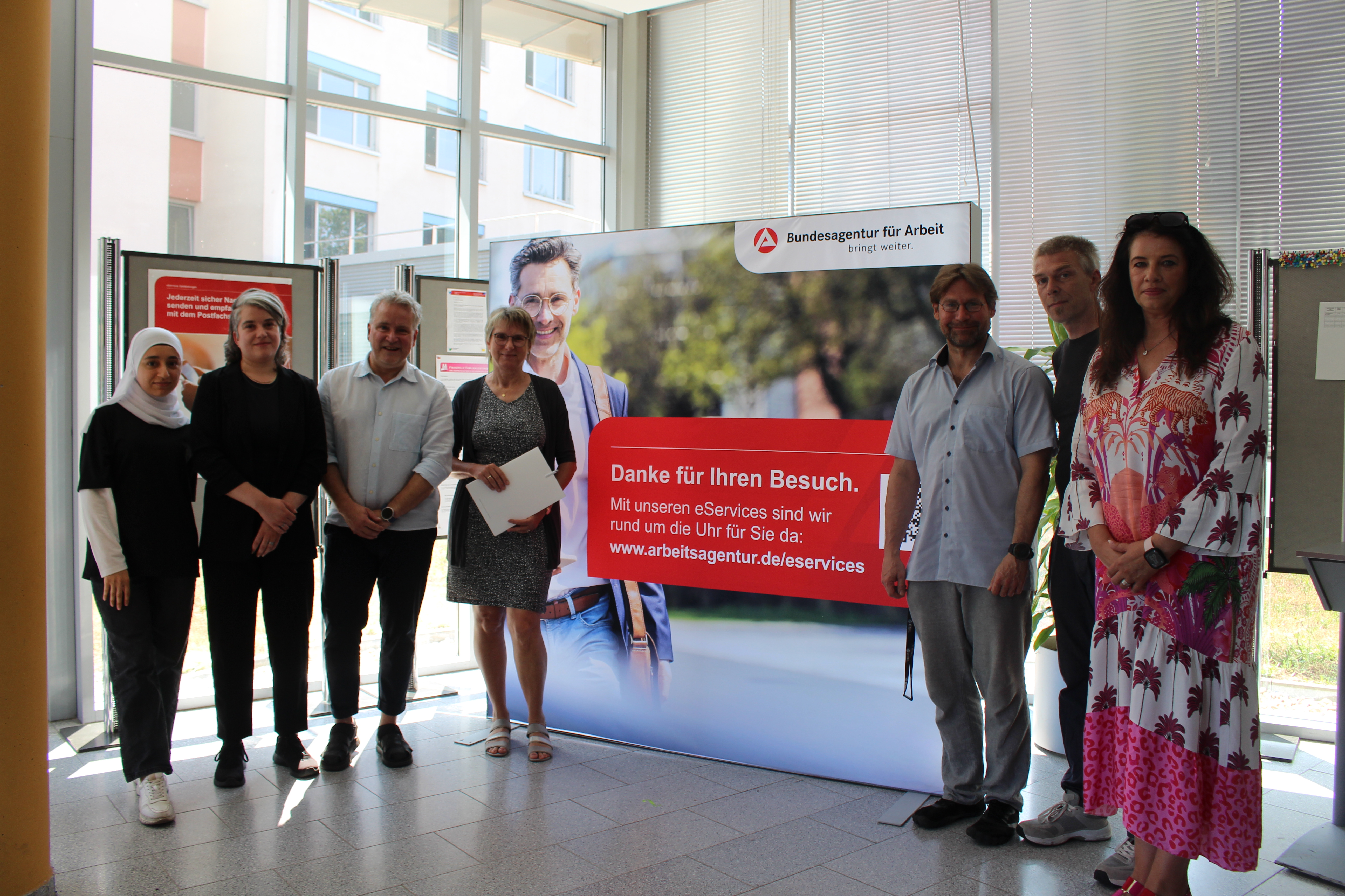 Mehrere Menschen stehen vor einem riesigen Banner der Bundesagentur für Arbeit.